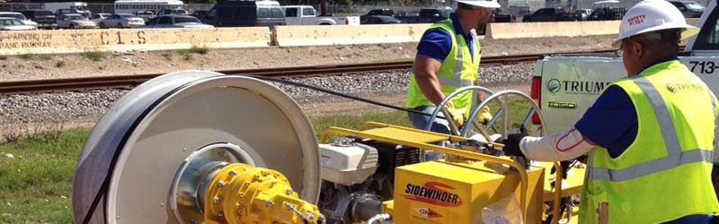 Triumph technicians in high-visibility vests feeding cable from a reel at a jobsite