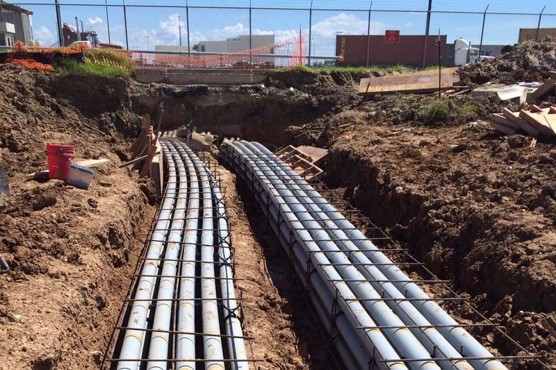 Banked rows of conduit laid in a long open trench, ready for encasement
