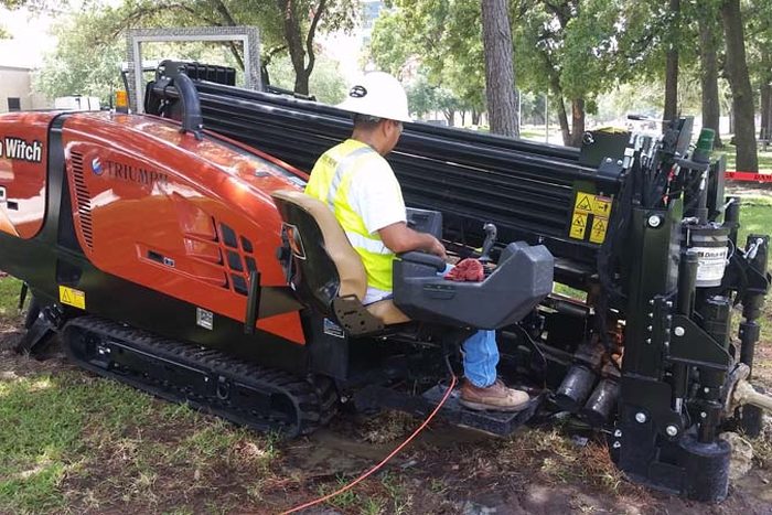 Triumph operator running a tracked Ditch Witch directional drilling rig on a grass verge