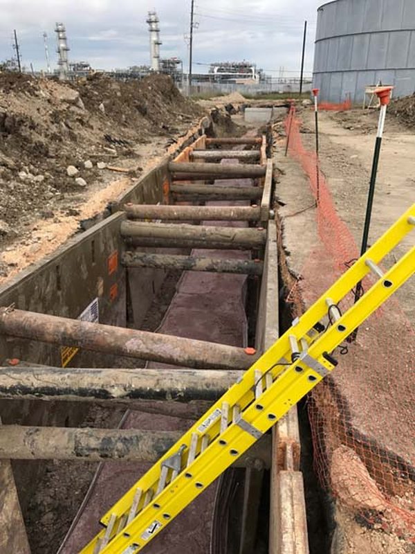 Shored trench with conduit runs in the bottom and a ladder set for access