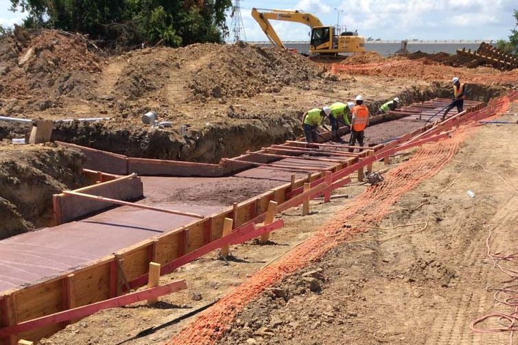 Crew and excavator working a shored trench alongside a stockpile of spoil